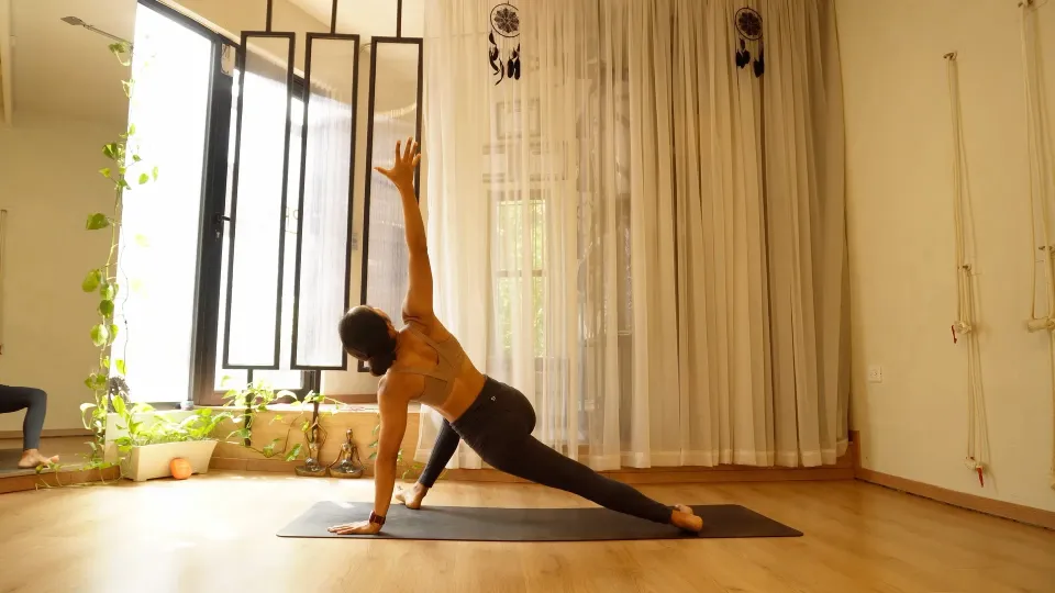 Instructora en postura de ángulo lateral extendido sobre su tapete en el estudio PRĀPTI, con luz natural y cuerdas de Kurunta en la pared